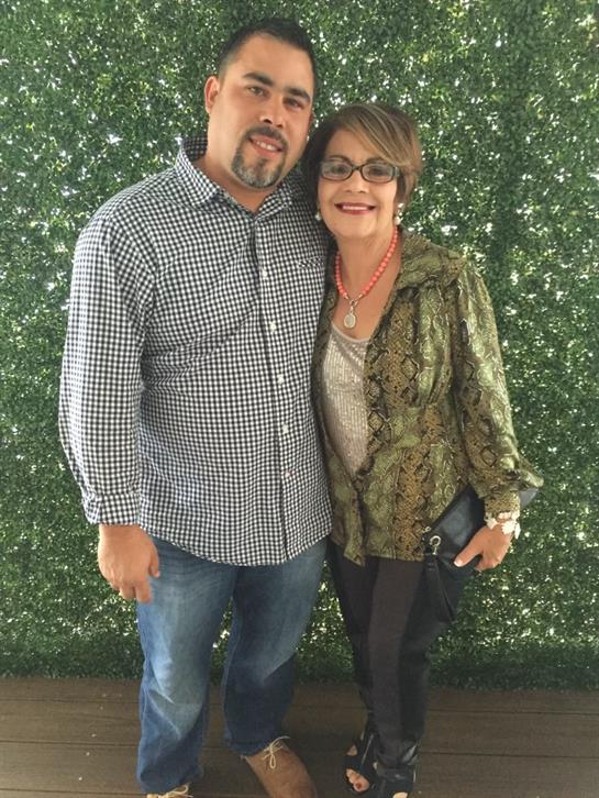 A couple smiles happily in front of a lush green background at a joyful event.