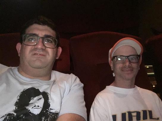 Two friends sit comfortably in a theater, watching a film and sharing a moment.