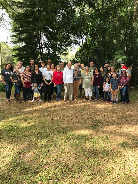 Group of people smiling and posing outdoors in a green garden during a warm, sunny afternoon.