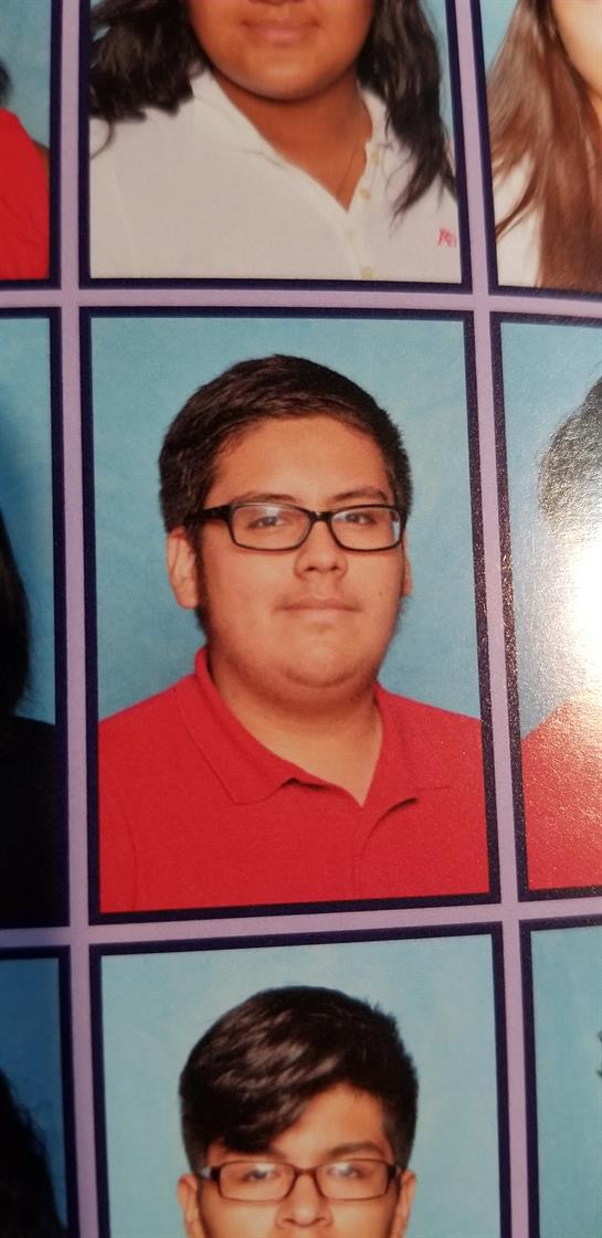 A young student is captured in a school portrait, smiling softly, wearing glasses and a red shirt.