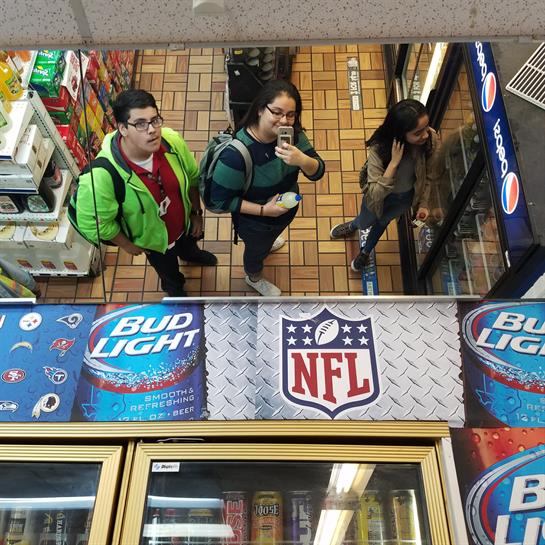 Three young adults capture a moment with a selfie while browsing drinks in a store.