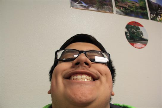 A boy smiles broadly while taking a selfie in a classroom, showcasing his excitement.