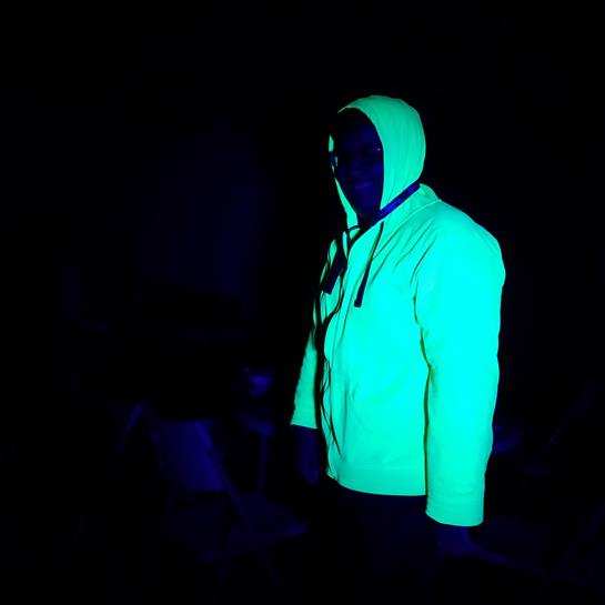 A person in a bright hoodie stands in a dimly lit area, creating a striking contrast.