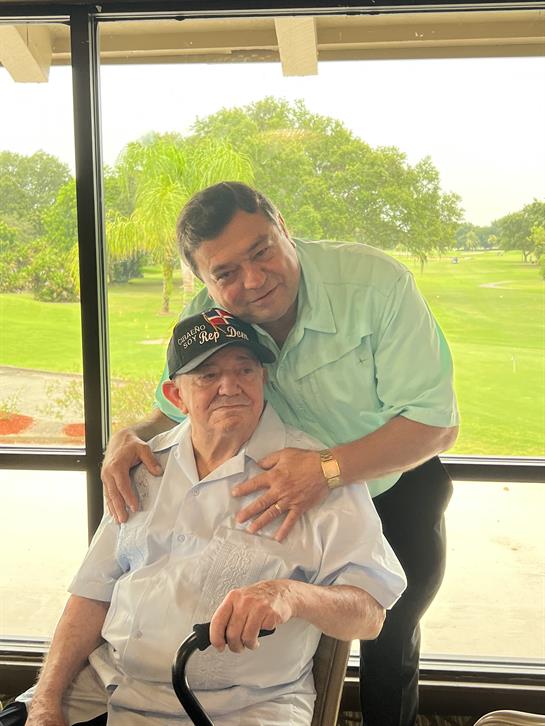 A man embraces his elderly father, both sharing a joyful moment in a sunny garden.