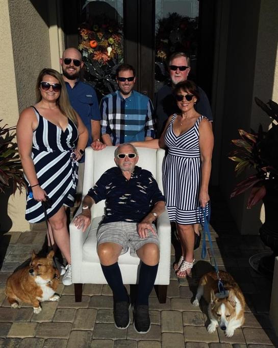 Family members pose together with a seated elder and dogs in a vibrant outdoor setting.