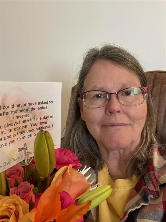 Joyful woman smiles while holding a vibrant bouquet of flowers and a thoughtful card in her home.