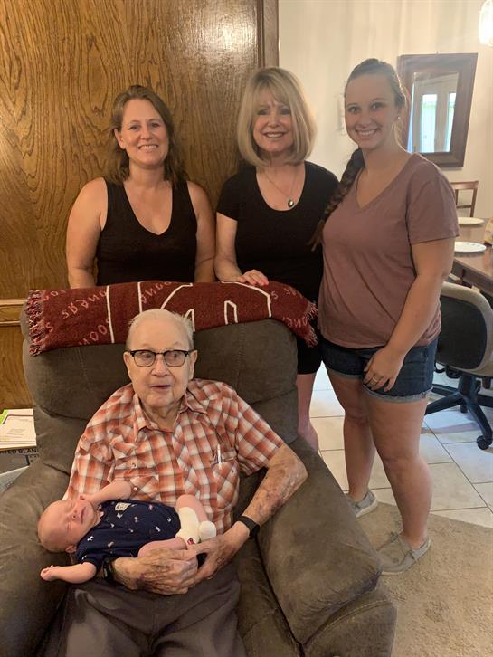 Family members smile happily while posing with a baby in a comfortable living room environment.
