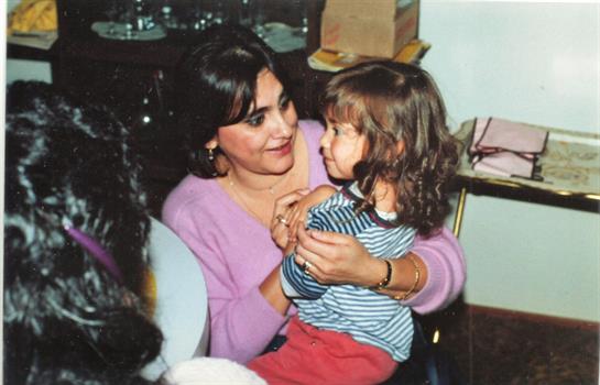 A happy mother holds her young daughter close at a family gathering, sharing joyful moments.