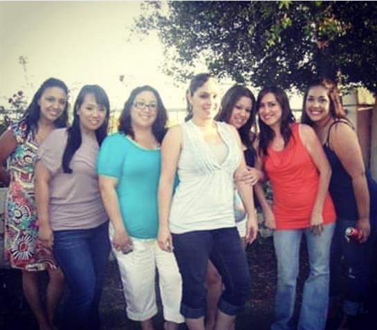 Eight friends pose together, smiling and enjoying a bright day outdoors by the water.