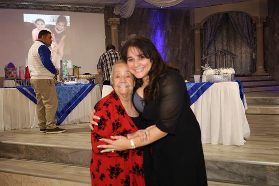 Two women share a heartfelt moment at a festive gathering, embracing each other joyfully.