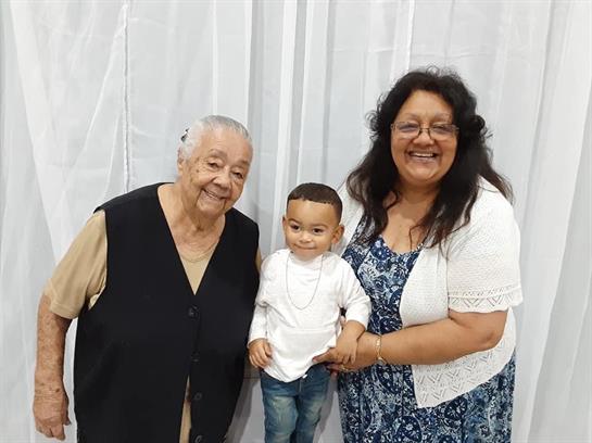 Three family members, a senior woman, an adult woman, and a young child, share smiles together.