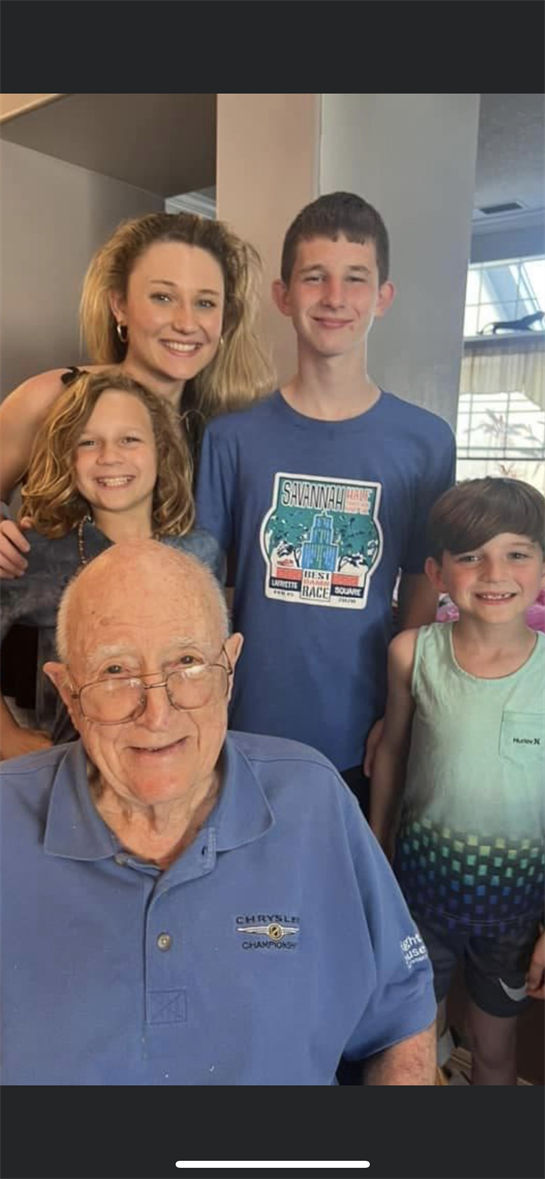 Four children pose happily with an elderly man, all smiling in a bright, cheerful room.