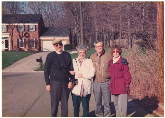 Four friends stand together outside a brick house with trees in the background on a winter day.