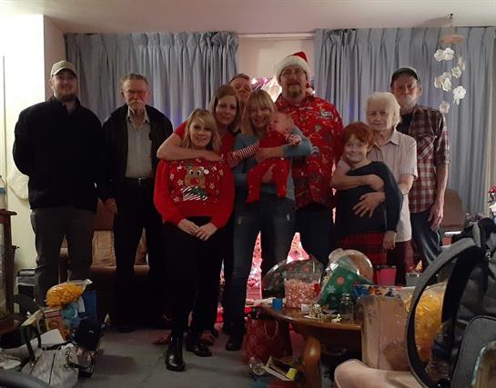 A large family poses together in festive attire, surrounded by holiday decorations and gifts.