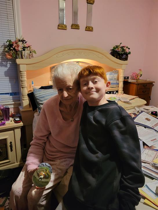 In a cozy bedroom, an elderly woman and a young boy sit together, sharing a joyful moment.