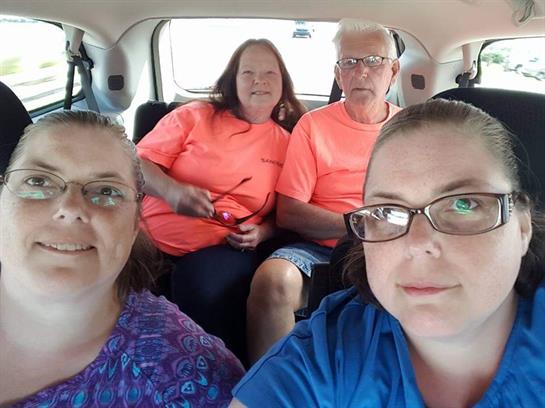 Four individuals in bright clothing share smiles while seated inside a vehicle, enjoying their trip.