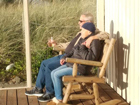 A couple sits together on a wooden deck, savoring a relaxing moment while watching nature.
