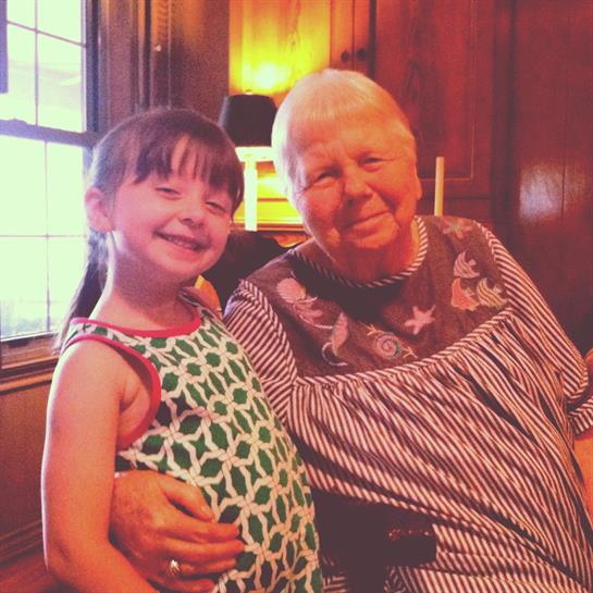 A senior woman smiles warmly next to a young girl in a cozy indoor setting.