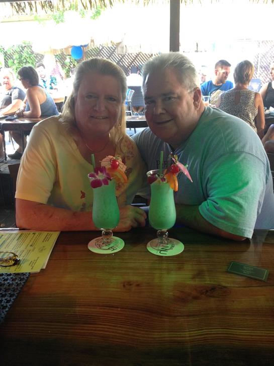 A couple smiles at a bar, sipping tropical cocktails with friends around them.