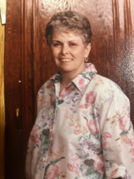 A woman stands smiling in a floral blouse in a cozy indoor setting during a social event.