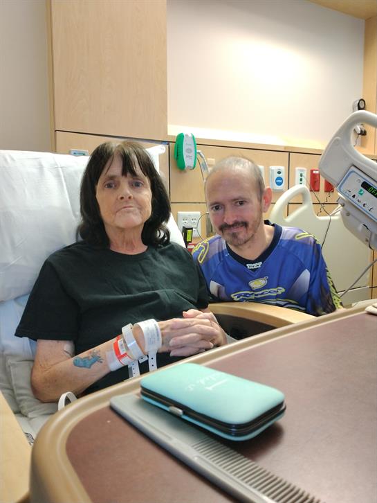 A man visits a woman in a hospital bed, both sharing a warm moment together.