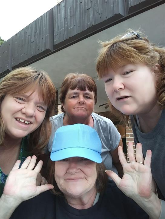 Friends pose together with joyful expressions, showing playful hand gestures in a bright setting.