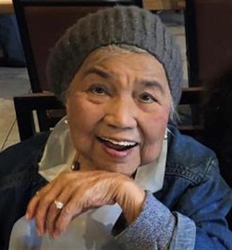 Elderly woman with bright smile and knit hat enjoys company at a cafe table during daytime.