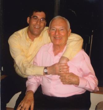 Two men are smiling and hugging, enjoying their time together in a relaxed indoor environment.