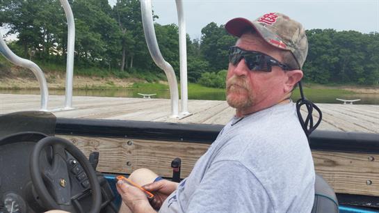 A man enjoys a leisurely day on a boat, surrounded by lush greenery on a sunny summer afternoon.