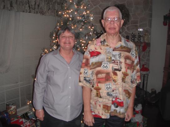 A cheerful couple stands in a warmly lit living room by a Christmas tree, celebrating the holidays.