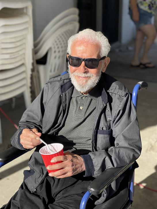 Senior man in sunglasses savors ice cream while seated in a wheelchair at a cafe outdoors.