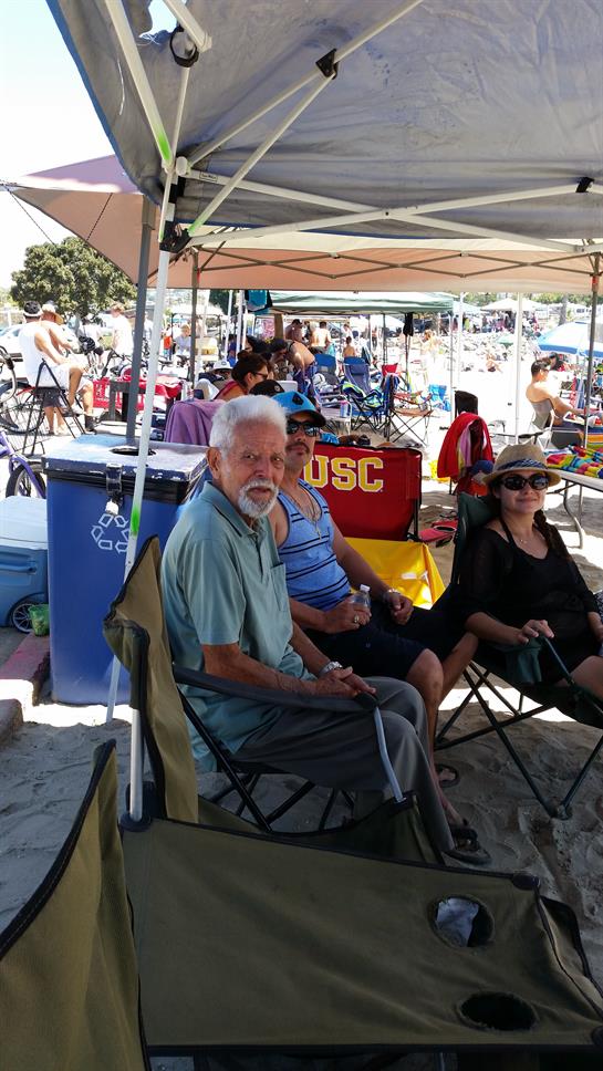Friends relax under tents on a sunny beach while others swim nearby.