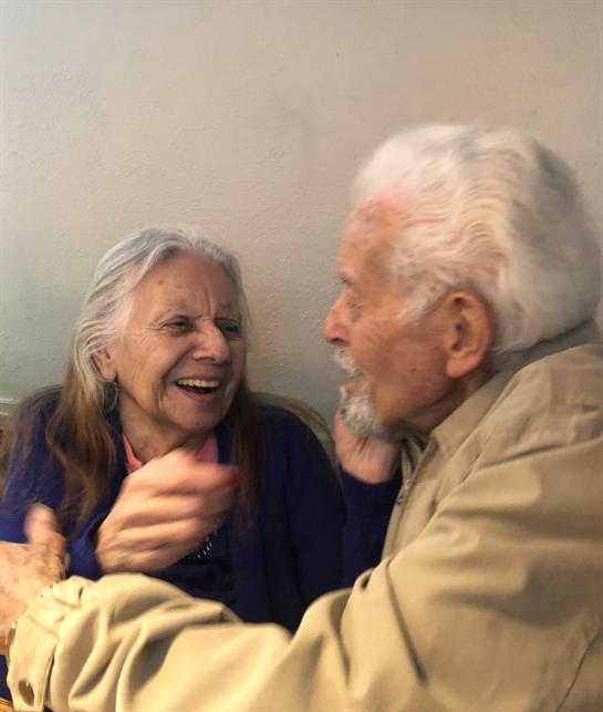 Two seniors engage in joyful conversation, smiling and reminiscing in a warm, intimate atmosphere.