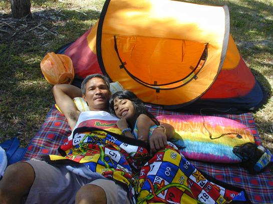 A couple shares a peaceful picnic on a colorful quilt by a cheerful tent.