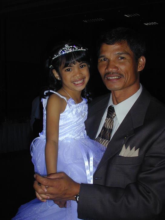 A smiling father holds his daughter in a lovely blue dress at a nighttime event.