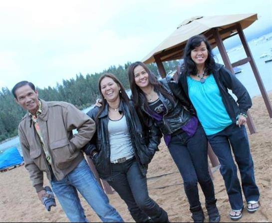 Friends stand together by the lake, smiling and enjoying their time on a cool, overcast day.