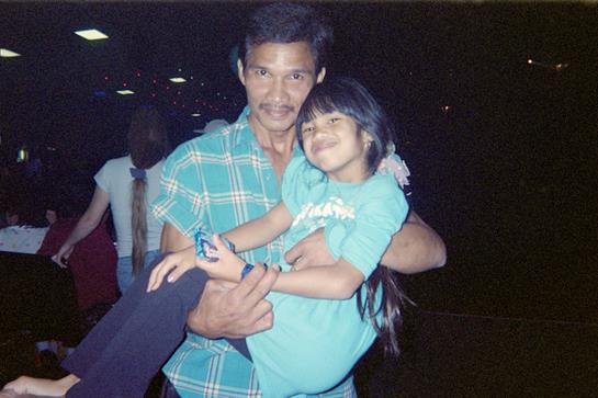 A joyful father lifts his smiling daughter in a park, showcasing their close bond in the evening.