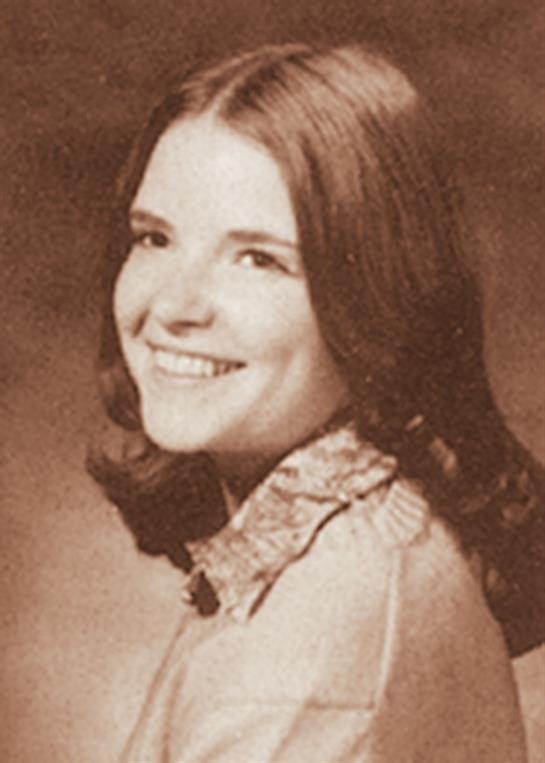 A smiling young woman with long hair poses for a classic studio portrait, exuding warmth.