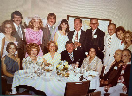 Twelve friends are gathered, enjoying drinks and laughter at a celebration.