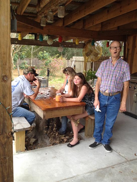 A group of four friends and family relaxes around a wooden table, sharing drinks and stories.