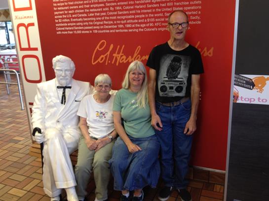 Friends gather to take a picture with a life-sized statue in a casual dining setting.