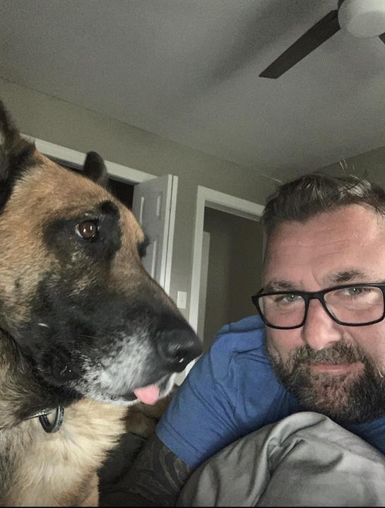A man relaxes at home, enjoying quality time with his dog while lying on a bed.