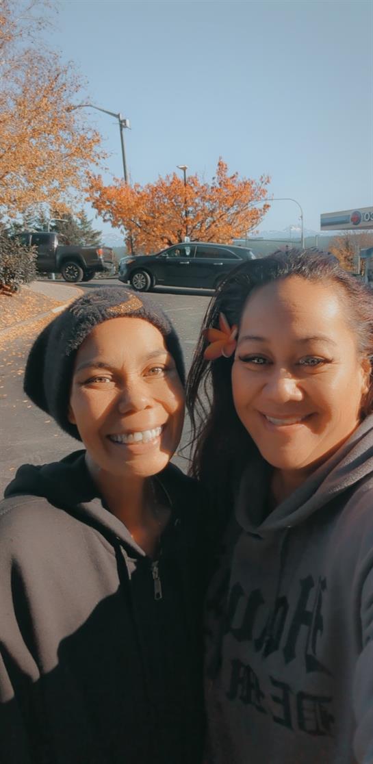 Two friends smile together, enjoying a warm autumn day surrounded by colorful leaves.