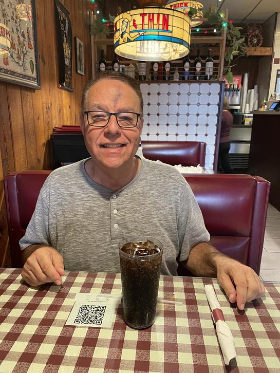 A man smiles while sitting at a booth in a restaurant holding a drink during lunchtime.
