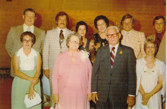 A lively family reunion takes place in a warmly lit hall, featuring diverse attire from the 1970s.