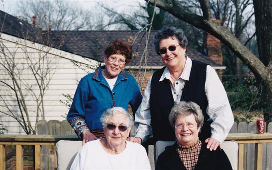 Group of four friends smiling together, dressed casually, sharing a joyful moment in the sun.