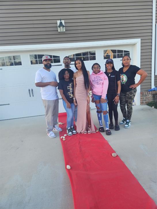 A family joyfully poses together on a red carpet at a celebration outside their home.