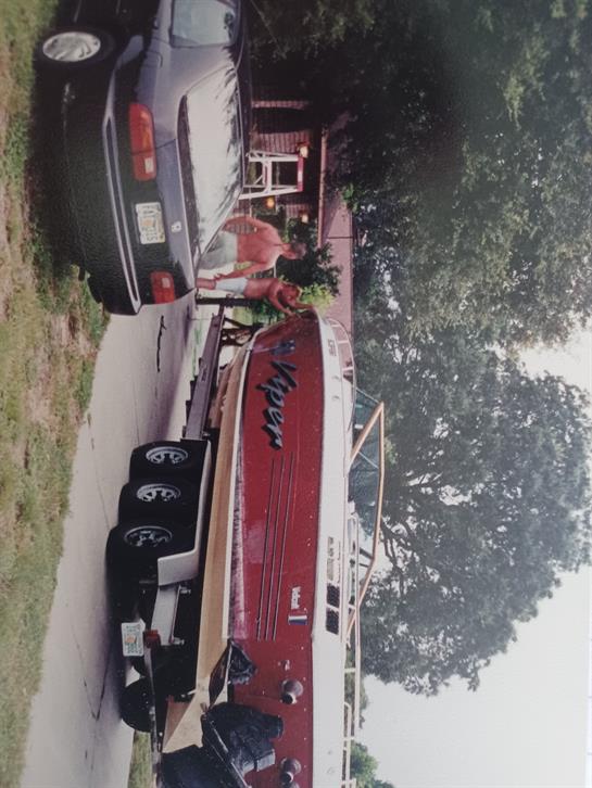 A man is getting ready to launch a red boat from a trailer, parked beside a black car.