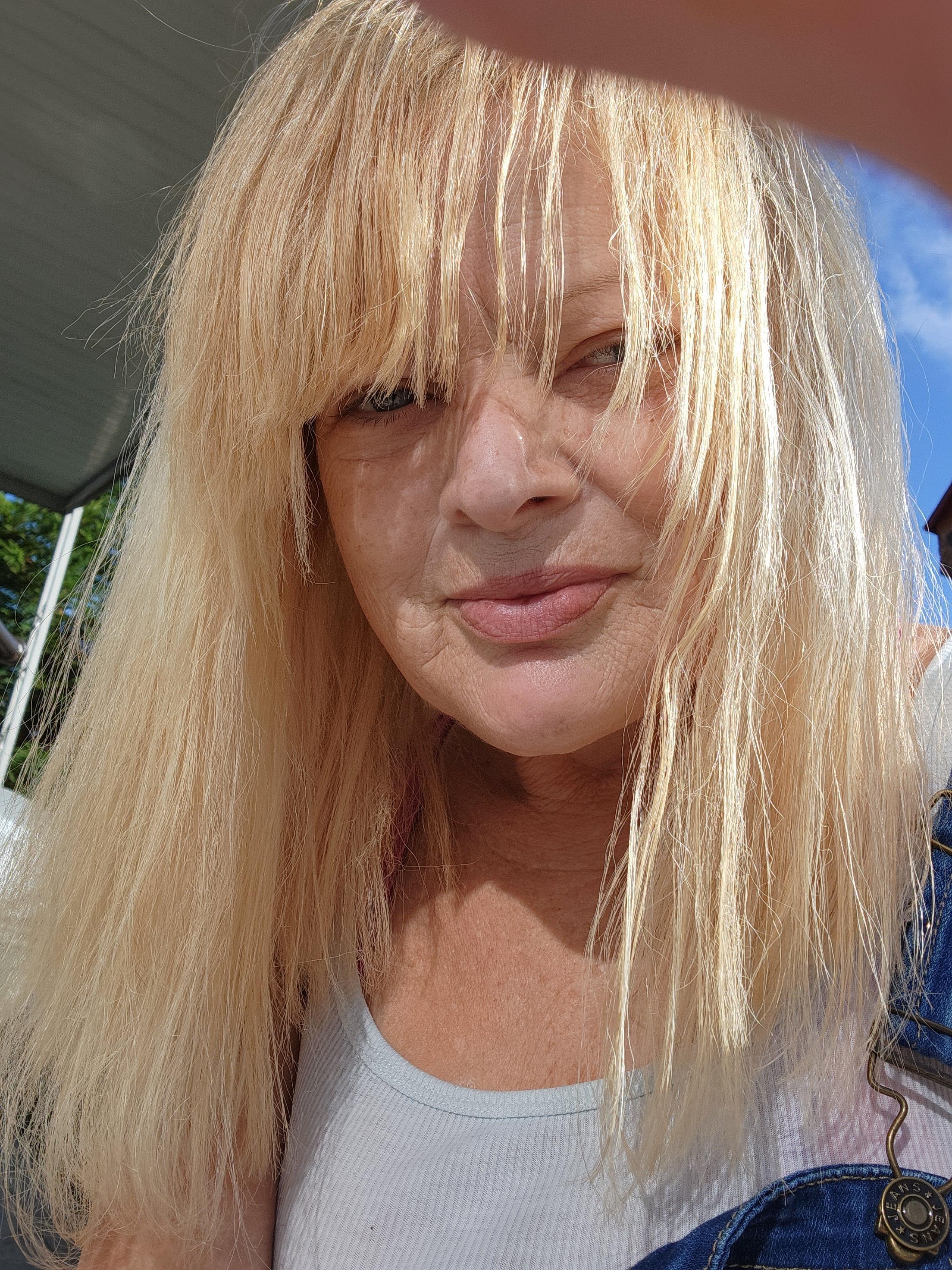 A woman with long blonde hair engages in a cheerful moment outside under clear skies.