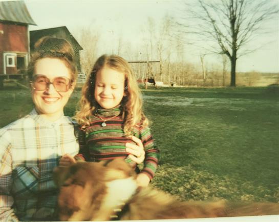 A woman and a young girl enjoy a sunny day outdoors, surrounded by nature and a dog.